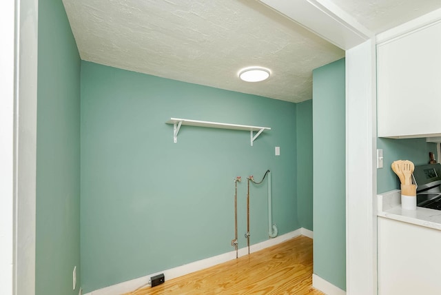 laundry room with laundry area, a textured ceiling, light wood-type flooring, and baseboards