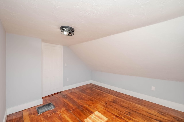 bonus room featuring wood finished floors, visible vents, baseboards, lofted ceiling, and a textured ceiling