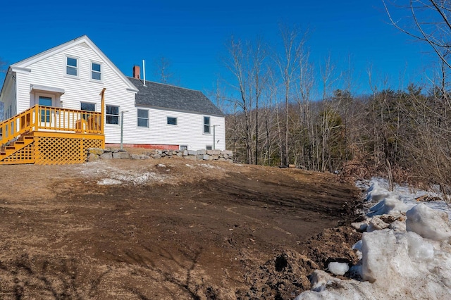 rear view of property featuring a deck, a chimney, and a shingled roof