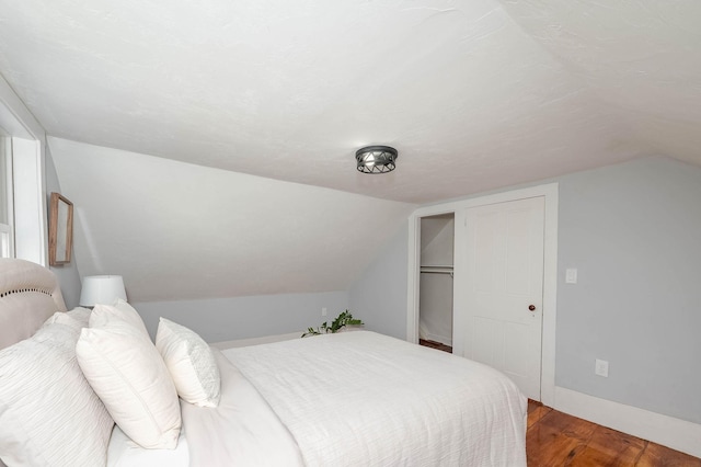 bedroom featuring a closet, vaulted ceiling, baseboards, and wood finished floors