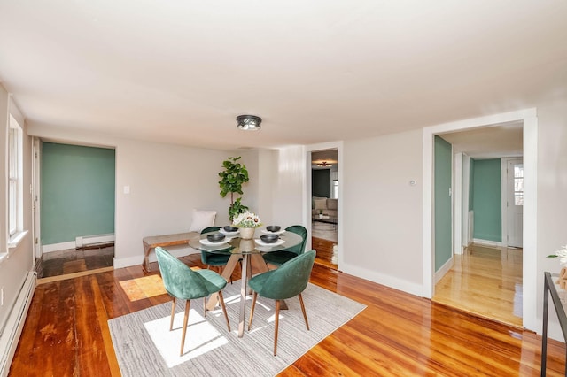 dining area with a baseboard heating unit, wood finished floors, and baseboards