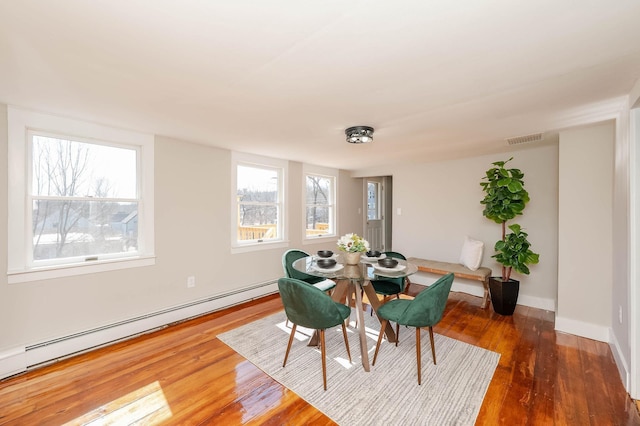 dining room with visible vents, a baseboard heating unit, baseboards, and wood finished floors