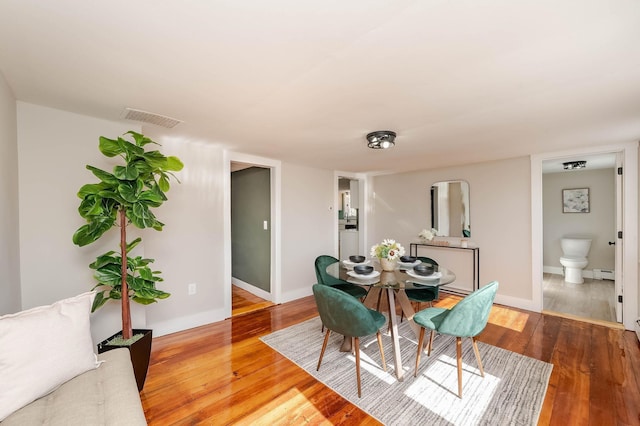 dining space with a baseboard heating unit, visible vents, wood finished floors, and baseboards