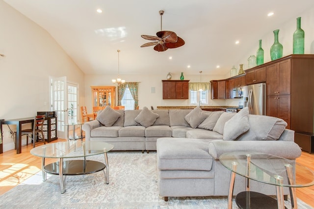 living area with ceiling fan with notable chandelier, high vaulted ceiling, and light wood-style floors