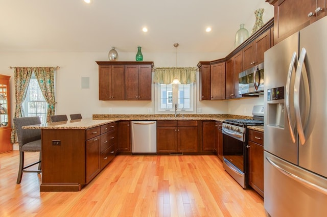 kitchen featuring a breakfast bar, a sink, light wood-style floors, appliances with stainless steel finishes, and a peninsula