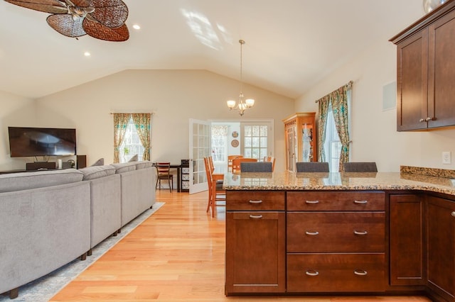 kitchen featuring pendant lighting, light wood-style floors, a peninsula, light stone countertops, and vaulted ceiling