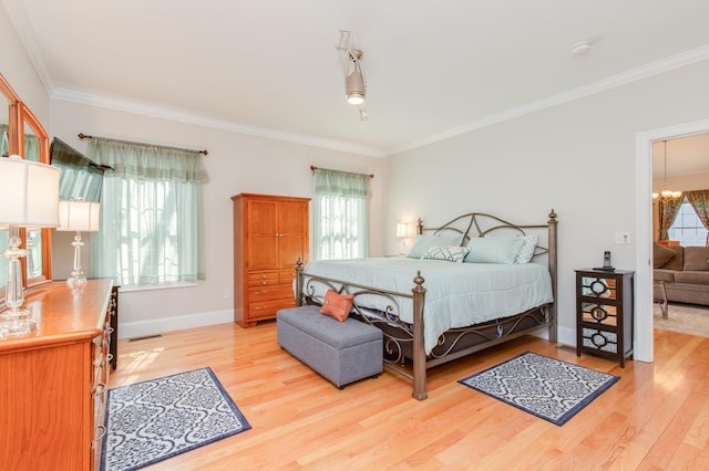 bedroom with an inviting chandelier, crown molding, light wood-style flooring, and baseboards