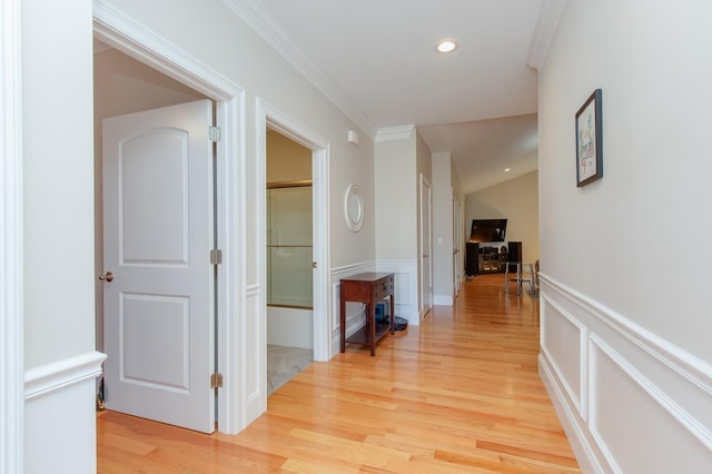 corridor with light wood finished floors, crown molding, a wainscoted wall, recessed lighting, and a decorative wall