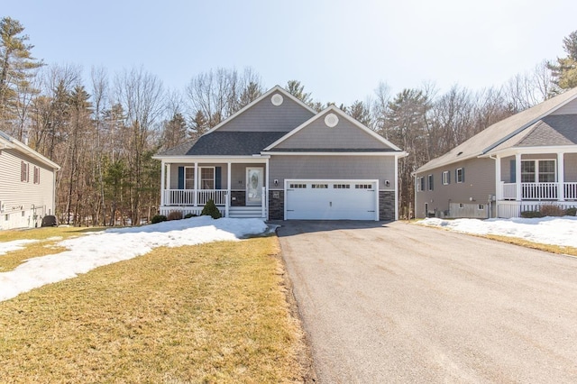 view of front of property featuring a lawn, driveway, stone siding, covered porch, and an attached garage