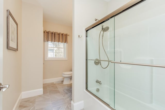 bathroom featuring toilet, baseboards, and combined bath / shower with glass door