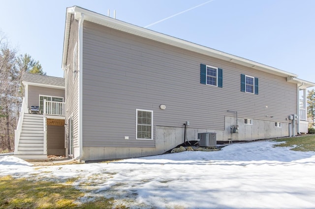 snow covered back of property with stairs and central AC