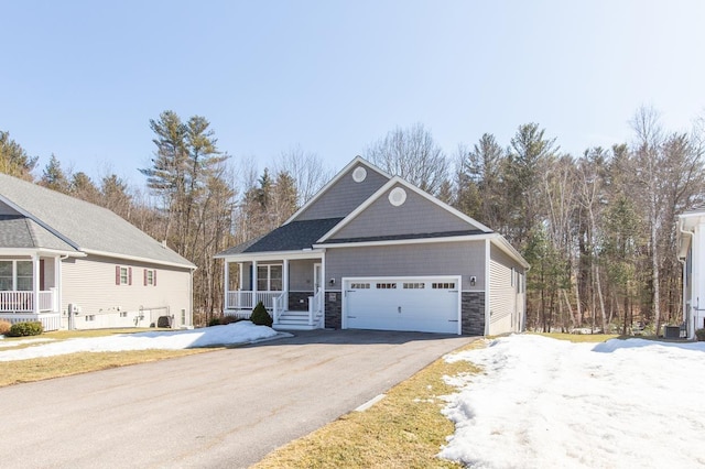 view of front of house with a porch, aphalt driveway, an attached garage, and stone siding