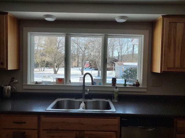 kitchen with stainless steel dishwasher, dark countertops, brown cabinetry, and a sink