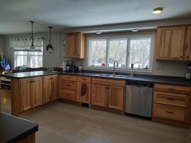 kitchen with stainless steel dishwasher, a peninsula, dark countertops, and a sink