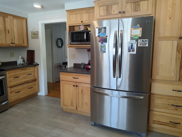 kitchen featuring stainless steel appliances, dark countertops, light floors, and light brown cabinets