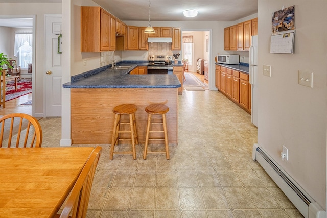 kitchen with dark countertops, under cabinet range hood, baseboard heating, white appliances, and a sink