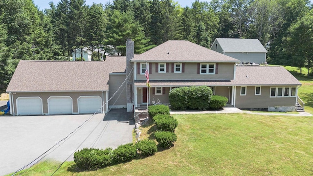 traditional-style home featuring a front lawn, aphalt driveway, roof with shingles, a chimney, and a garage