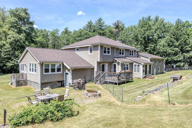 back of property with a yard, a fire pit, a deck, and a shingled roof