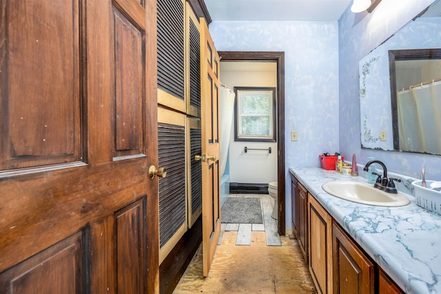 bathroom featuring a shower with curtain, toilet, wallpapered walls, baseboards, and vanity