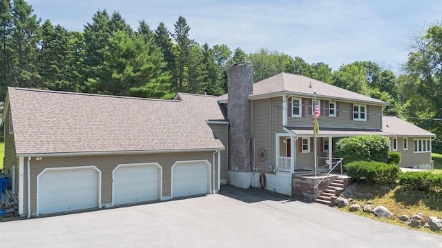 view of front facade featuring covered porch, driveway, a chimney, and roof with shingles