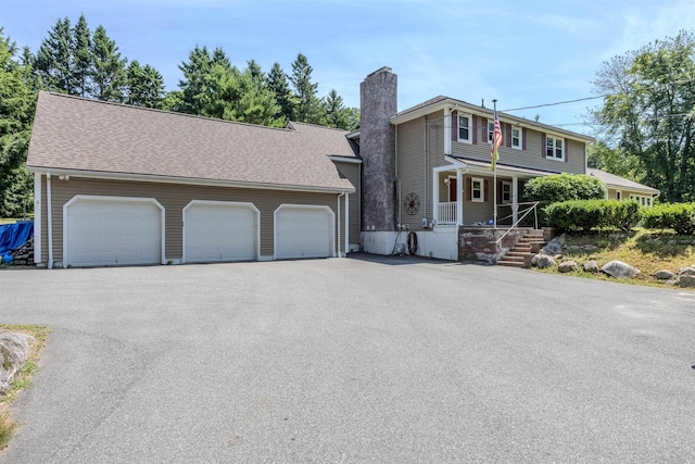 view of front of house with driveway, a porch, a chimney, and a shingled roof