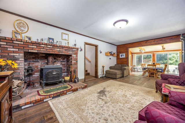 living room featuring a wood stove, dark wood-type flooring, crown molding, and stairway