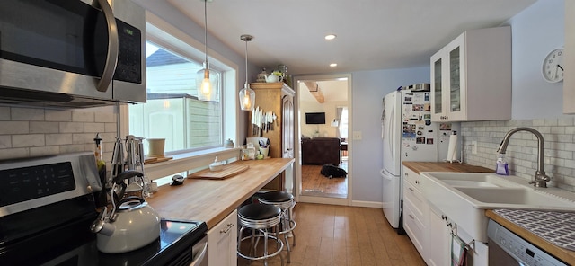 kitchen with glass insert cabinets, butcher block counters, appliances with stainless steel finishes, white cabinets, and a sink