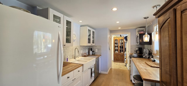 kitchen with wooden counters, freestanding refrigerator, a sink, glass insert cabinets, and light wood-type flooring