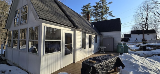 view of snowy exterior with a deck, a sunroom, and roof with shingles