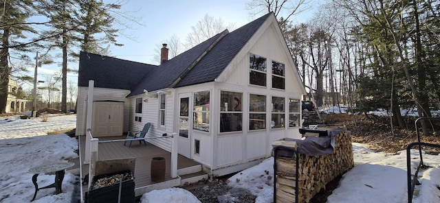 snow covered property with a sunroom, roof with shingles, and a chimney