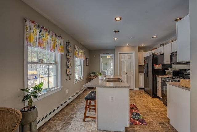 kitchen featuring a sink, a kitchen bar, an island with sink, black appliances, and a baseboard radiator