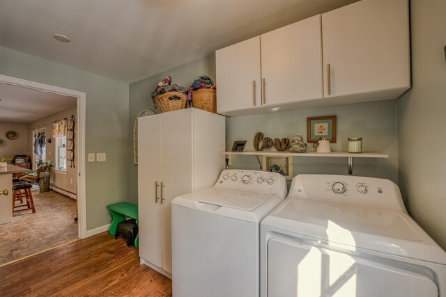 clothes washing area featuring light wood-type flooring, washer and dryer, cabinet space, a baseboard radiator, and baseboards