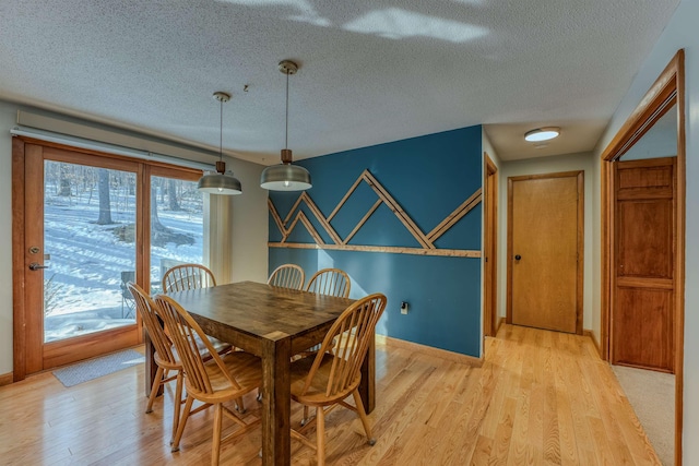 dining space featuring a textured ceiling, baseboards, and light wood-style floors