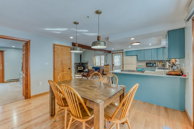 dining area with a baseboard radiator, baseboards, light wood-style floors, and a wood stove