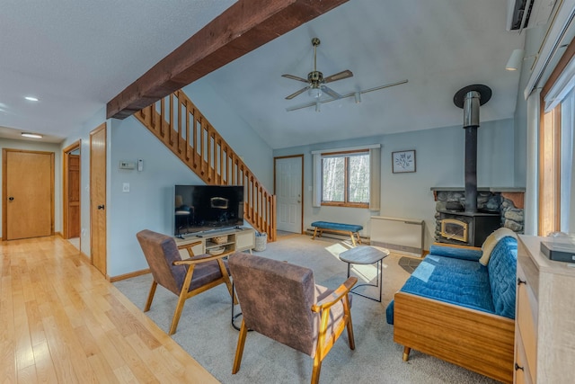 living area featuring a ceiling fan, hardwood / wood-style flooring, stairs, baseboards, and a wood stove