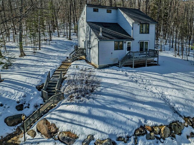 snow covered back of property featuring stairs, a deck, and roof with shingles