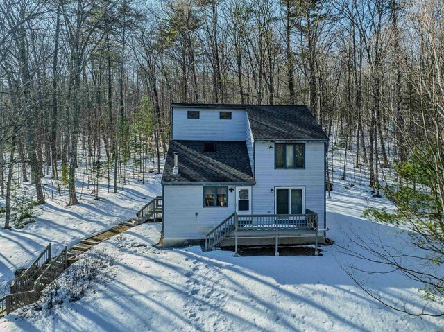 snow covered rear of property featuring stairs, roof with shingles, and a wooden deck