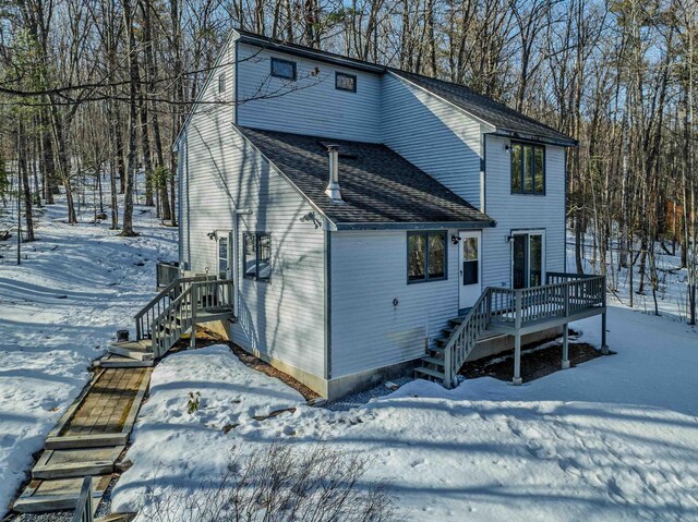 snow covered back of property featuring a shingled roof and a deck