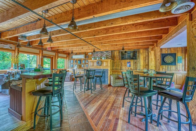 dining area featuring beamed ceiling, visible vents, an AC wall unit, wooden walls, and a dry bar