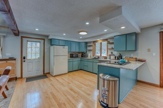 kitchen with a sink, light wood-style flooring, a peninsula, freestanding refrigerator, and open shelves