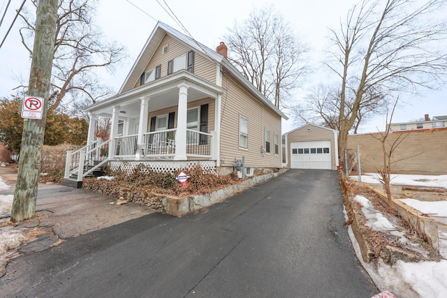 view of front facade with aphalt driveway, a porch, a chimney, a garage, and an outbuilding