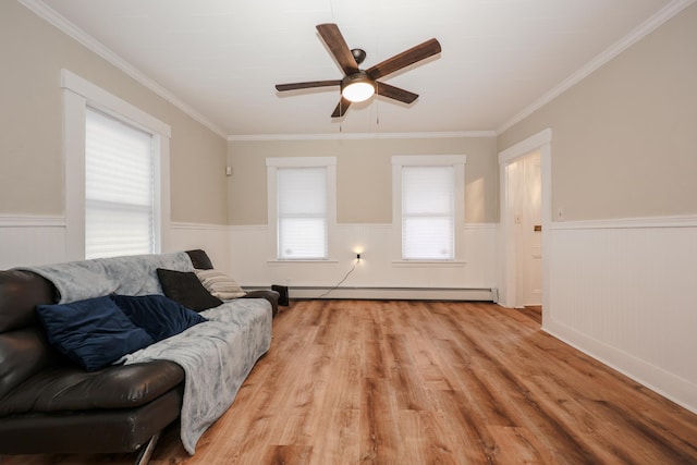 living area with a baseboard heating unit, light wood-style flooring, wainscoting, and ornamental molding