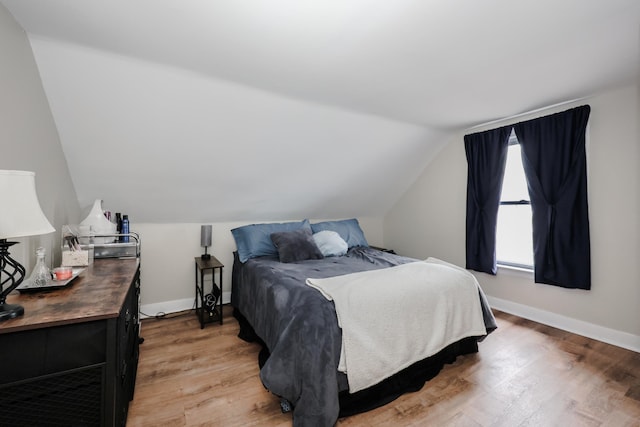 bedroom featuring baseboards, light wood-style flooring, and vaulted ceiling