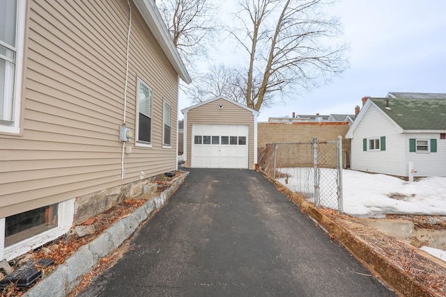 view of home's exterior with aphalt driveway, a detached garage, an outdoor structure, and fence