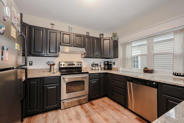 kitchen with under cabinet range hood, light stone counters, light wood-style floors, and appliances with stainless steel finishes