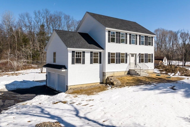 colonial home featuring aphalt driveway, an attached garage, and a shingled roof