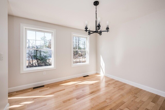 unfurnished dining area featuring an inviting chandelier, light wood-style flooring, visible vents, and baseboards