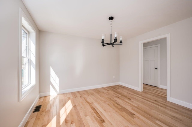 unfurnished room with light wood finished floors, visible vents, a notable chandelier, and baseboards