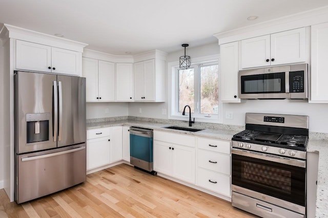 kitchen with light stone counters, light wood-style flooring, appliances with stainless steel finishes, white cabinetry, and a sink