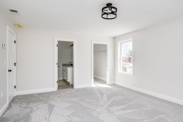 unfurnished bedroom with visible vents, light carpet, ensuite bath, baseboards, and a spacious closet